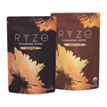 Two stand-up pouches of RYZE Mushroom Coffee on a plain white background. The left pouch is dark brown with black and gold leaf-like graphics and reads 'RYZE MUSHROOM COFFEE Rich & Robust.